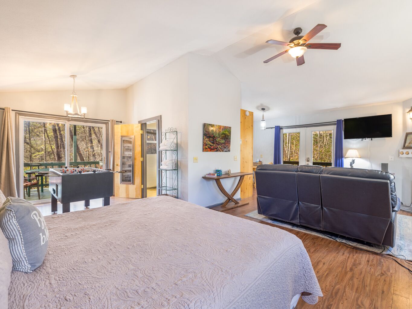 A bedroom with a bed, a sofa, a foosball table, a ceiling fan, and a TV.