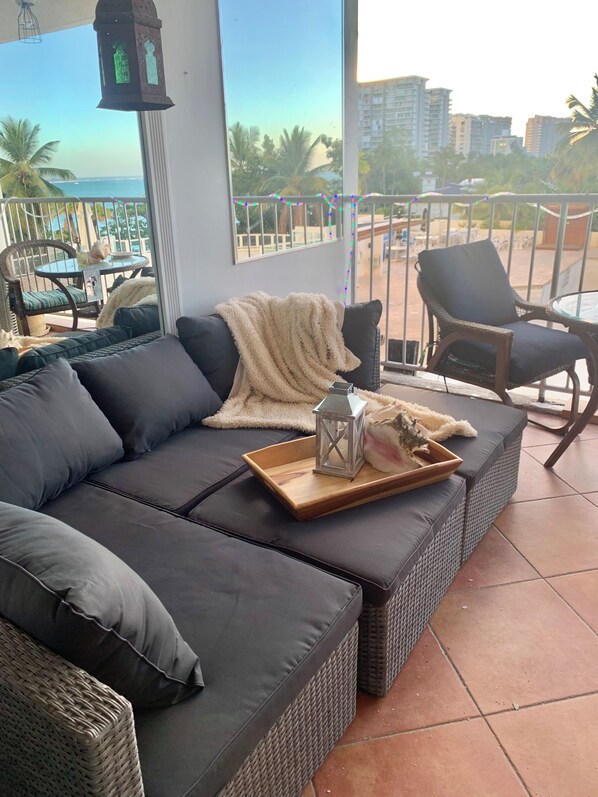 A balcony with a dark-colored sofa, wicker furniture, and a small table with a lantern and decorative items.