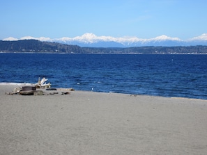 Ein Strand mit einem felsigen Bereich und einer Aussicht auf schneebedeckte Berge in der Ferne.