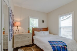 A bedroom with a wooden bed, a bedside lamp, a dresser, and two windows with blinds.