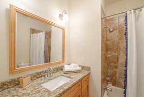 A bathroom with a marble sink, wooden vanity, a large mirror, a shower with a glass door, and a towel rack.
