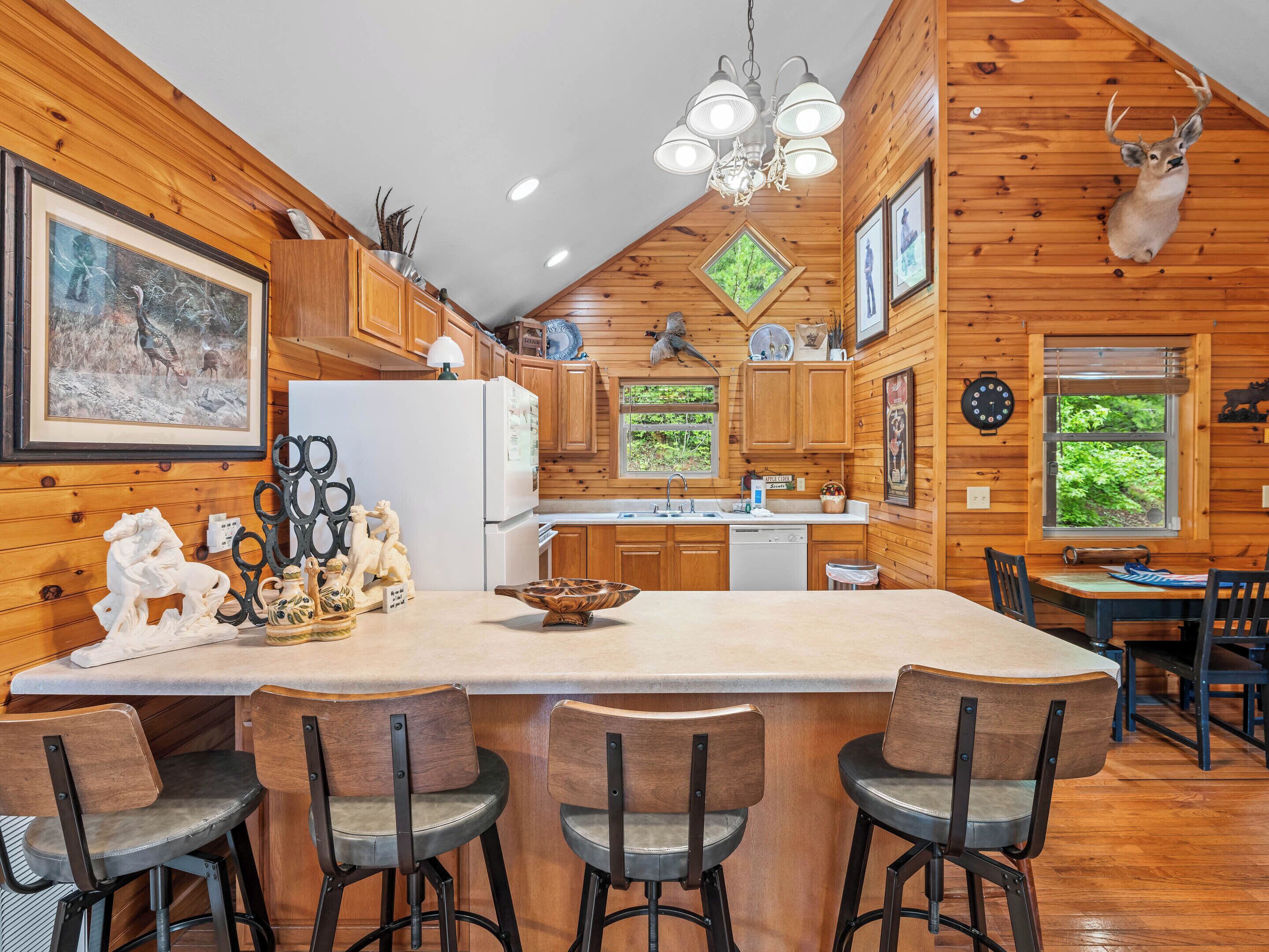 Una cocina de estilo cabaña con paredes de madera, una isla central con taburetes de bar, un refrigerador y un ciervo montado en la pared.