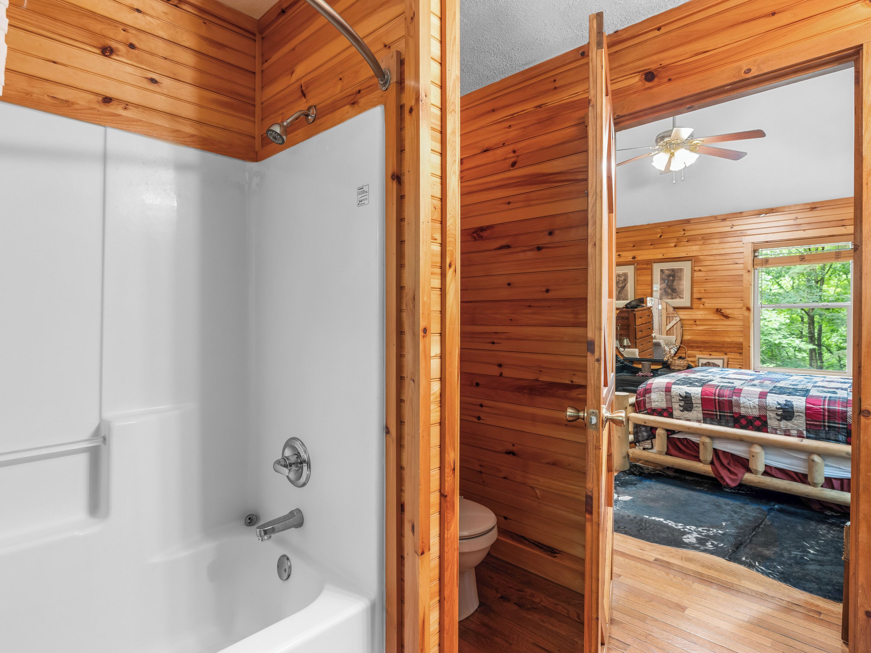Ein Badezimmer in einer Holzhütte mit Badewanne, Toilette und einem Bett mit karierter Bettdecke.