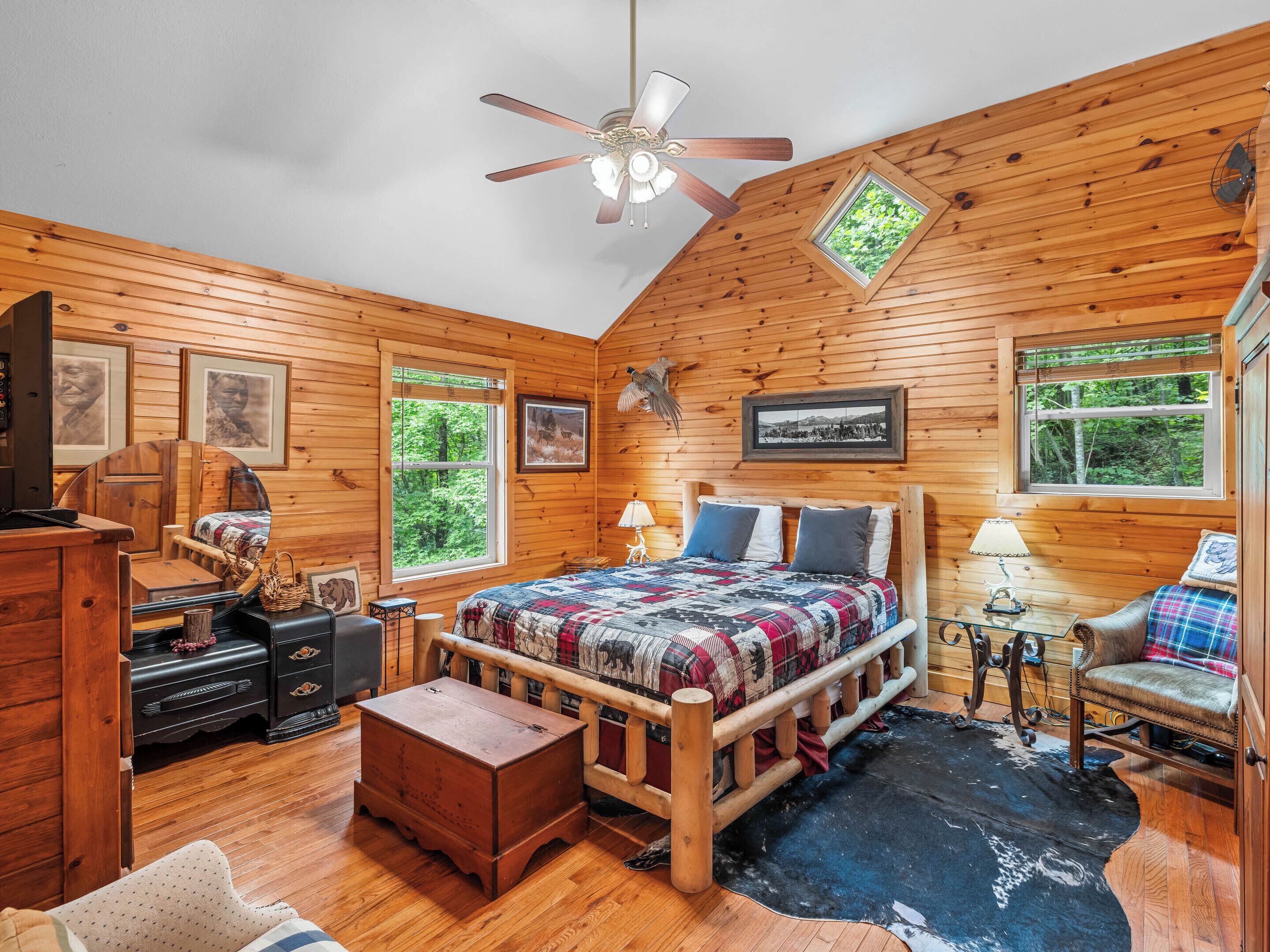A cozy log cabin bedroom with a wooden bed, a ceiling fan, and framed pictures on the walls.
