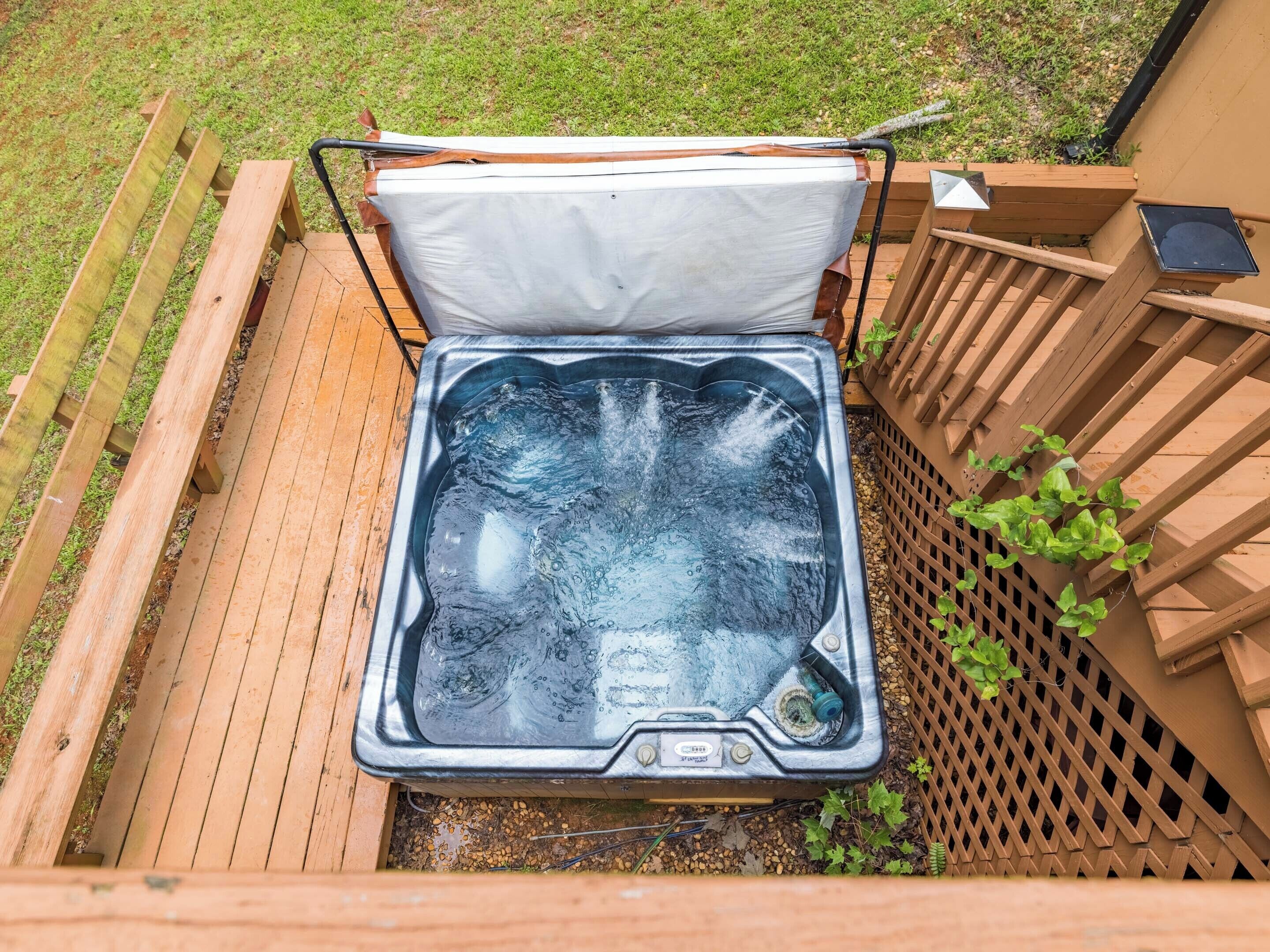 A hot tub with a cover, surrounded by a wooden deck and a wooden fence.