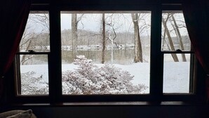 A room with a large window overlooking a snowy landscape with trees and bushes. - Stepping Stone Cabin (Page County)