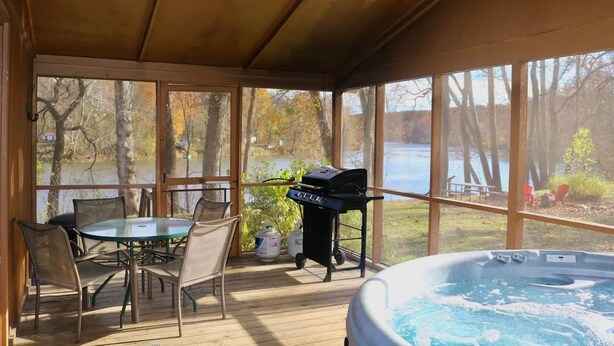 A covered outdoor area with a hot tub, a grill, and a table with chairs. - Stepping Stone Cabin (Page County)