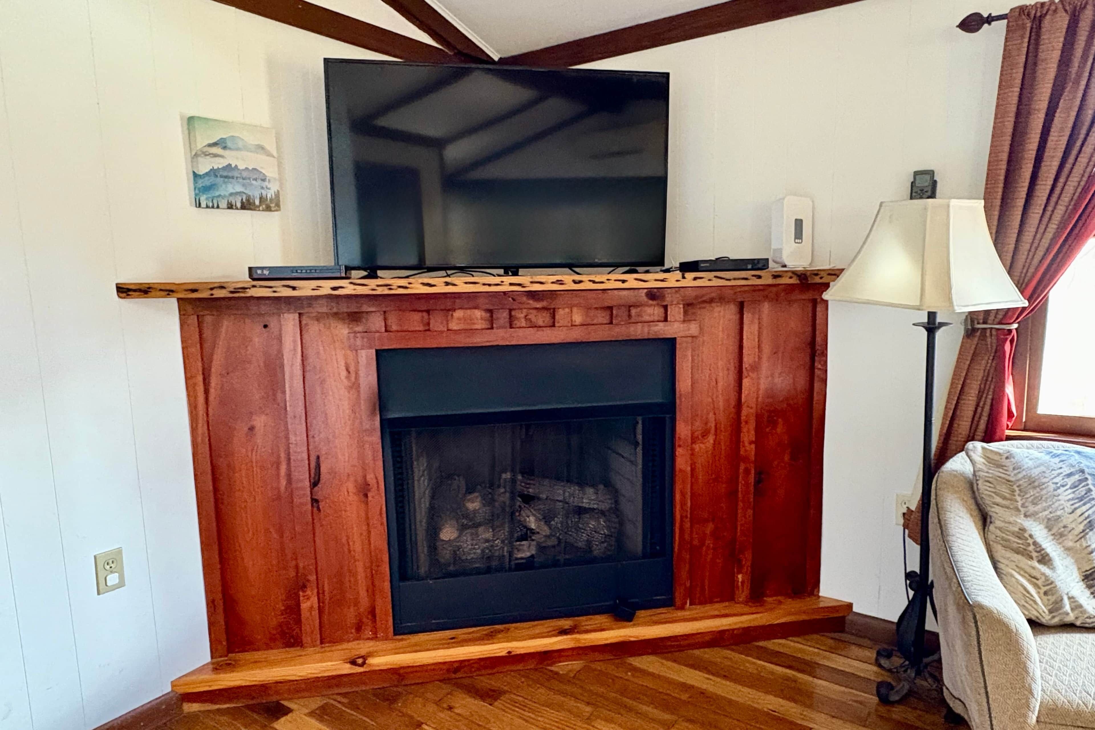 A fireplace with a wooden mantel, a television mounted above it, and a lamp to the right.