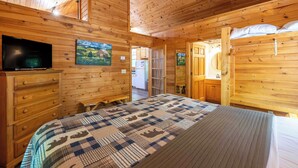 A wooden cabin interior with a bed, a TV, and a painting on the wall. - Bear Hug - Endorsed by Theodore Bear, a.k.a. "Teddy" (Sautee Nacoochee)