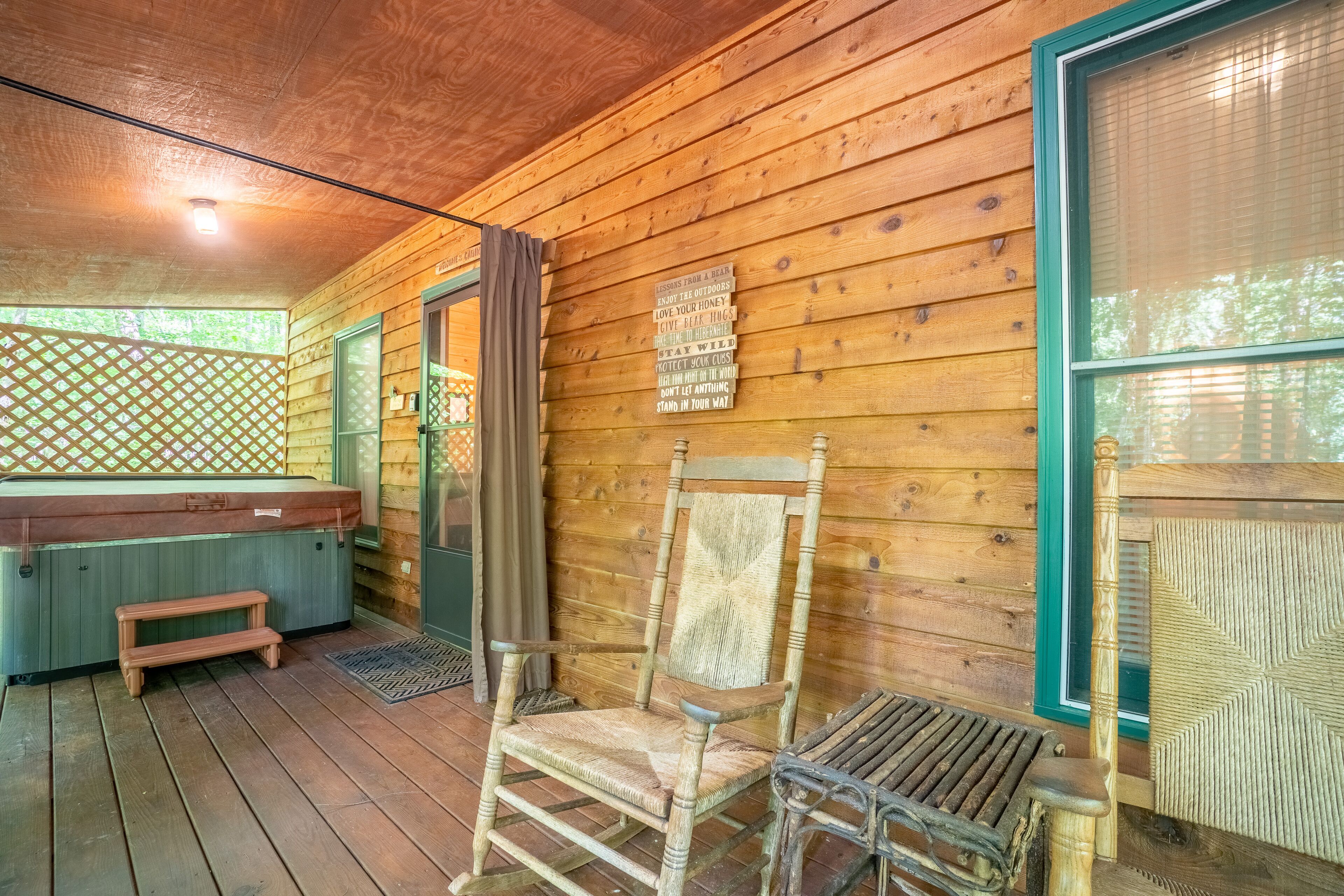 A wooden cabin with a hot tub, a wooden chair, and a bench on the porch.
