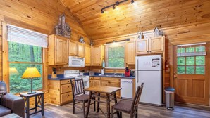 A wooden cabin kitchen with a dining table, chairs, a microwave, a refrigerator, and a sink. - Bear Hug - Endorsed by Theodore Bear, a.k.a. "Teddy" (Sautee Nacoochee)