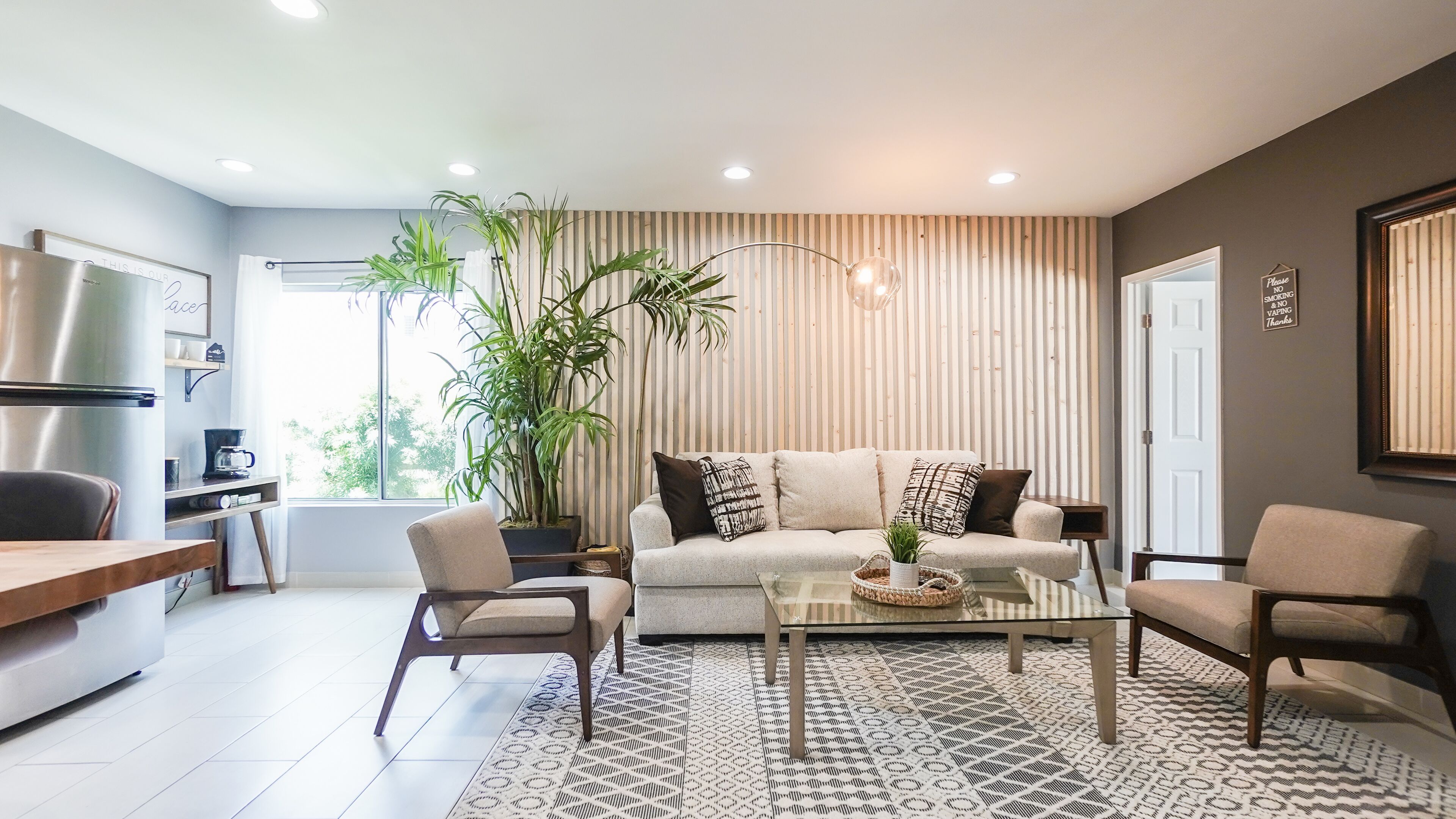 Una sala de estar moderna con un sofá, dos sillones, una mesa de centro y una planta grande.