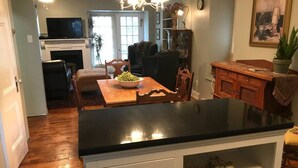 A kitchen with a black countertop, wooden cabinets, and a dining area with a table and chairs. - Vineyard Mansion - Carriage House - 1 Queen 1 Full Bed (St Joseph)