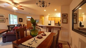 Ein Essbereich mit Holztisch, Stühlen und einer Vase mit Blumen. Ein Deckenventilator und eine Chandelier sind ebenfalls vorhanden.