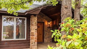 A rustic cabin with a stone chimney, a wooden door, and a large window. - Luxurious cabin in the 💚 of town.  Construction near. (Broken Bow)
