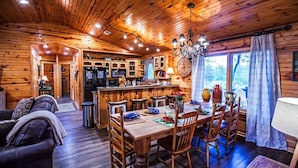 A cozy cabin interior with a wooden dining area, a kitchen, and a living room. - Luxurious cabin in the 💚 of town.  Construction near. (Broken Bow)