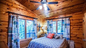 A cozy cabin bedroom with a wooden ceiling, a bed with patterned bedding, and curtains with geometric designs. - Luxurious cabin in the 💚 of town.  Construction near. (Broken Bow)