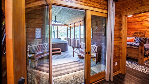A wooden cabin interior with a hot tub, seating area, and a view of the outdoors. - Luxurious cabin in the 💚 of town.  Construction near. (Broken Bow)