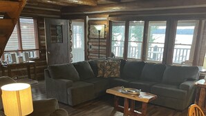 A cozy cabin interior with a wooden floor, a sectional sofa, a small table, and a lamp. - Lake Barkley Log Cabin Getaway + Free Weekday Pontoon (seasonal)  (Cadiz)