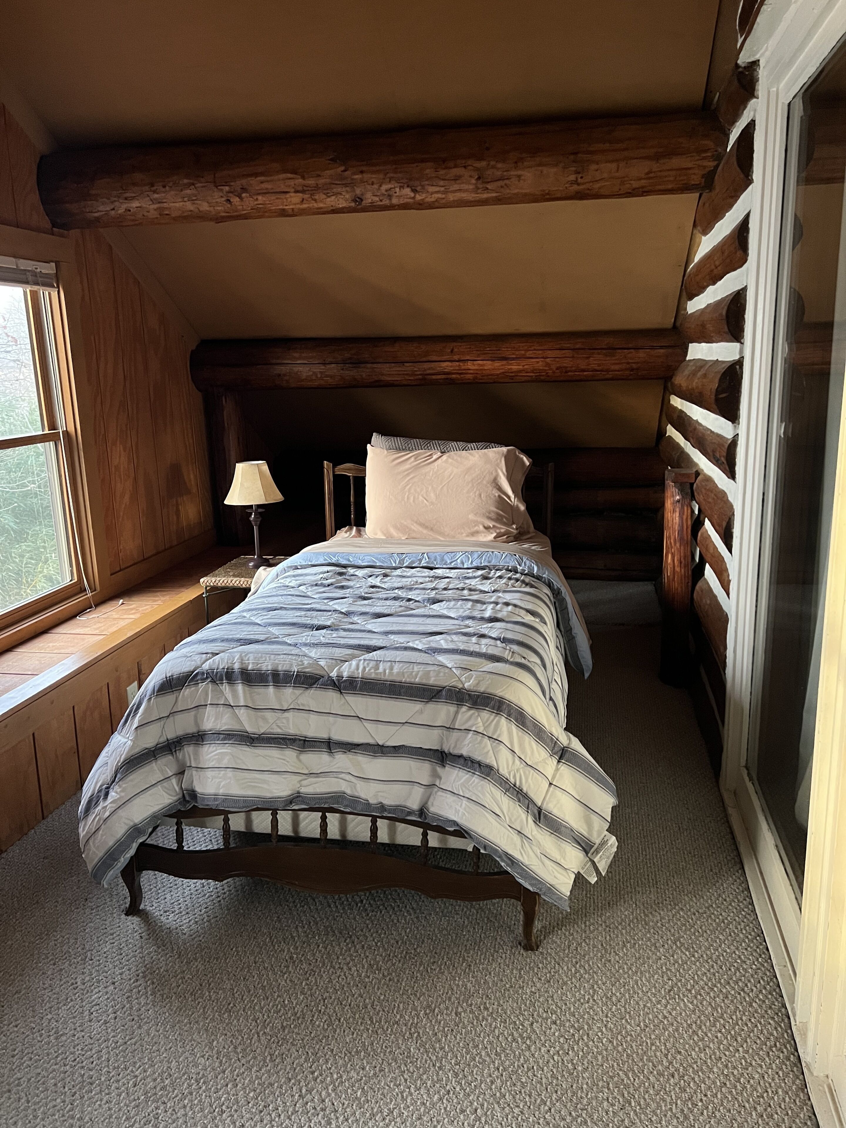 Un dormitorio con cama, lámpara y ventana.