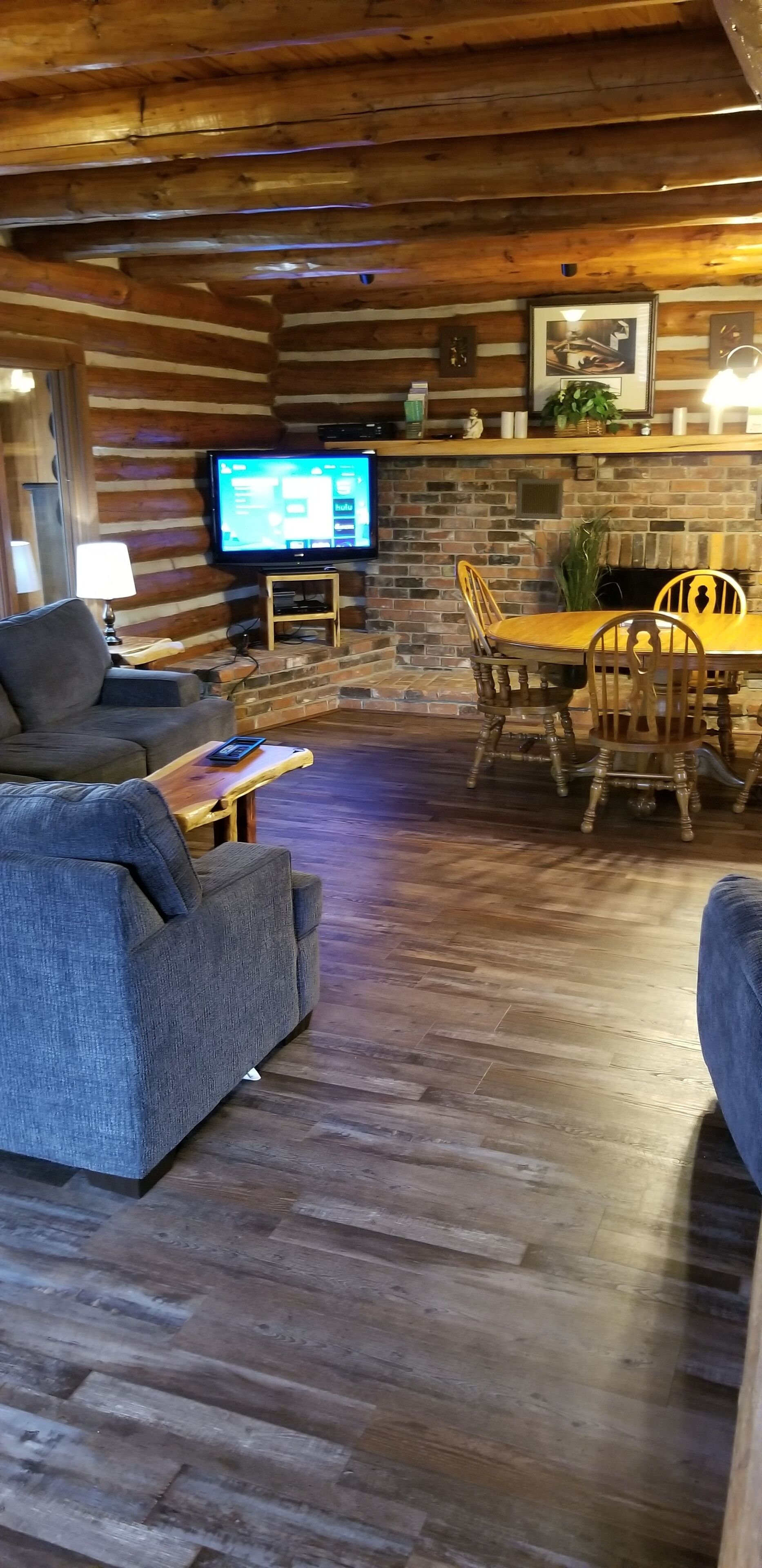 A cozy log cabin interior with a TV, wooden dining table, and comfortable seating.