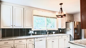 Una cocina con armarios blancos, un refrigerador de acero inoxidable y una ventana con persianas.