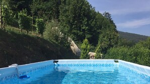 En swimmingpool med flisekant, omgivet af frodigt grønt og et kuperet landskab.