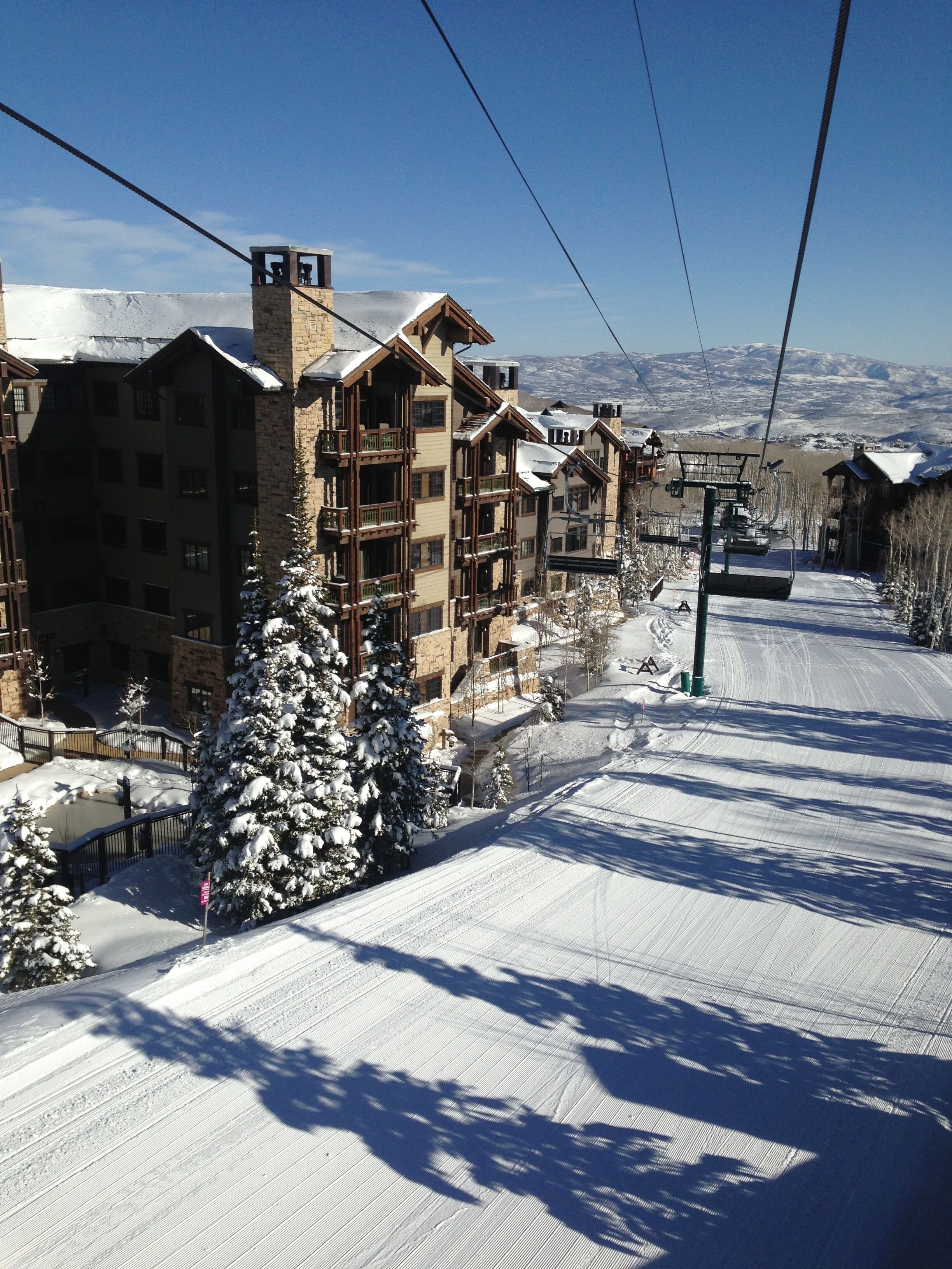 Ein mit Schnee bedeckter Skipisten mit Seilbahn, Gebäude mit Balkonen und ein schneebedeckter Baum.