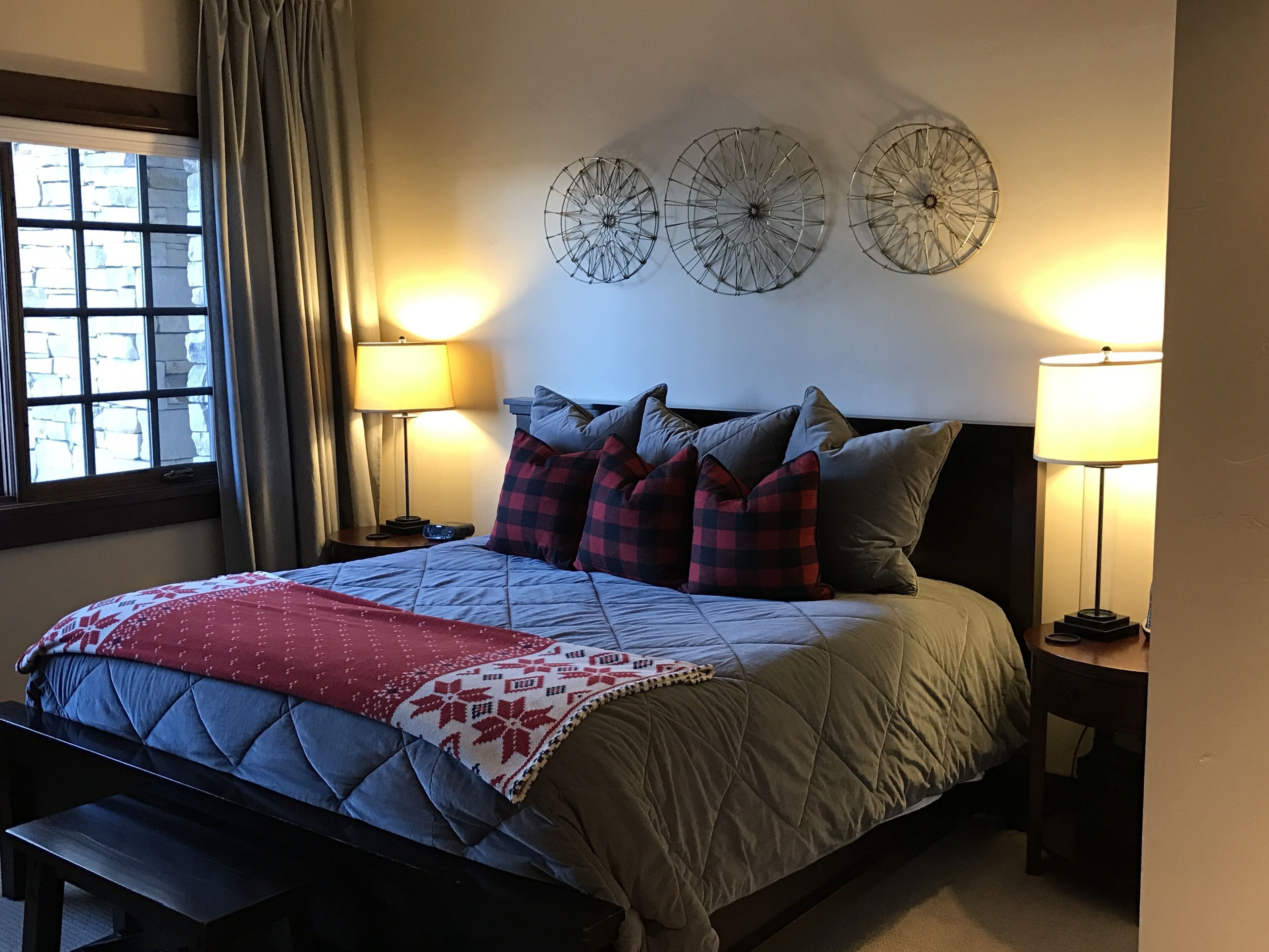 A bedroom with a bed, pillows, a bench, two bedside tables, and wall art.