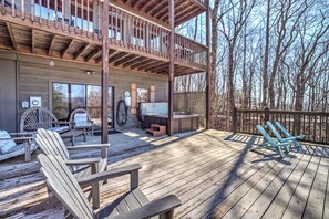 Relax on the deck with Adirondack chairs and a hot tub, surrounded by a wooded area.