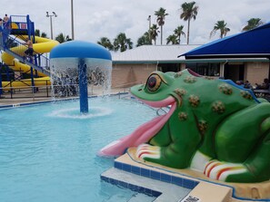 Une piscine agrémentée d’une grande fontaine en forme de grenouille et d’un toboggan jaune.