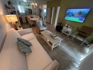 A living room with a sofa, coffee table, TV, and a dining area with chairs and a table.