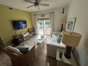 A living room with a sofa, a chair, a coffee table, a TV, a lamp, and a window with curtains.