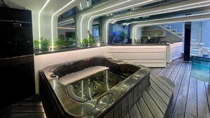 A modern interior with a hot tub, a kitchen area, and a staircase leading to an upper level.