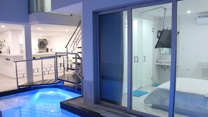A modern hotel room with a glass door leading to a bathroom, a small pool area, and a staircase to an upper level.