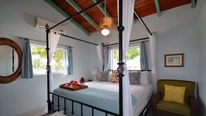 A four-poster bed with a canopy, a chair with a cushion, a bedside table with a tray, and a wall-mounted mirror. - Exceptional ocean views, centrally located, just 1,700 ft off Grace Bay Beach (Providenciales)