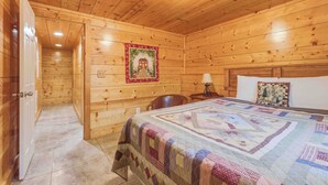 Una camera di una casetta in legno con un letto, un comodino, una lampada e una coperta trapuntata.