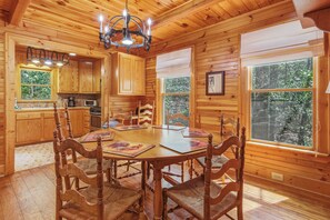 A wooden cabin interior with a dining table, chairs, a chandelier, and a kitchen area. - Knotty Pine - A Fairy Tale Cottage Getaway (Sautee Nacoochee)
