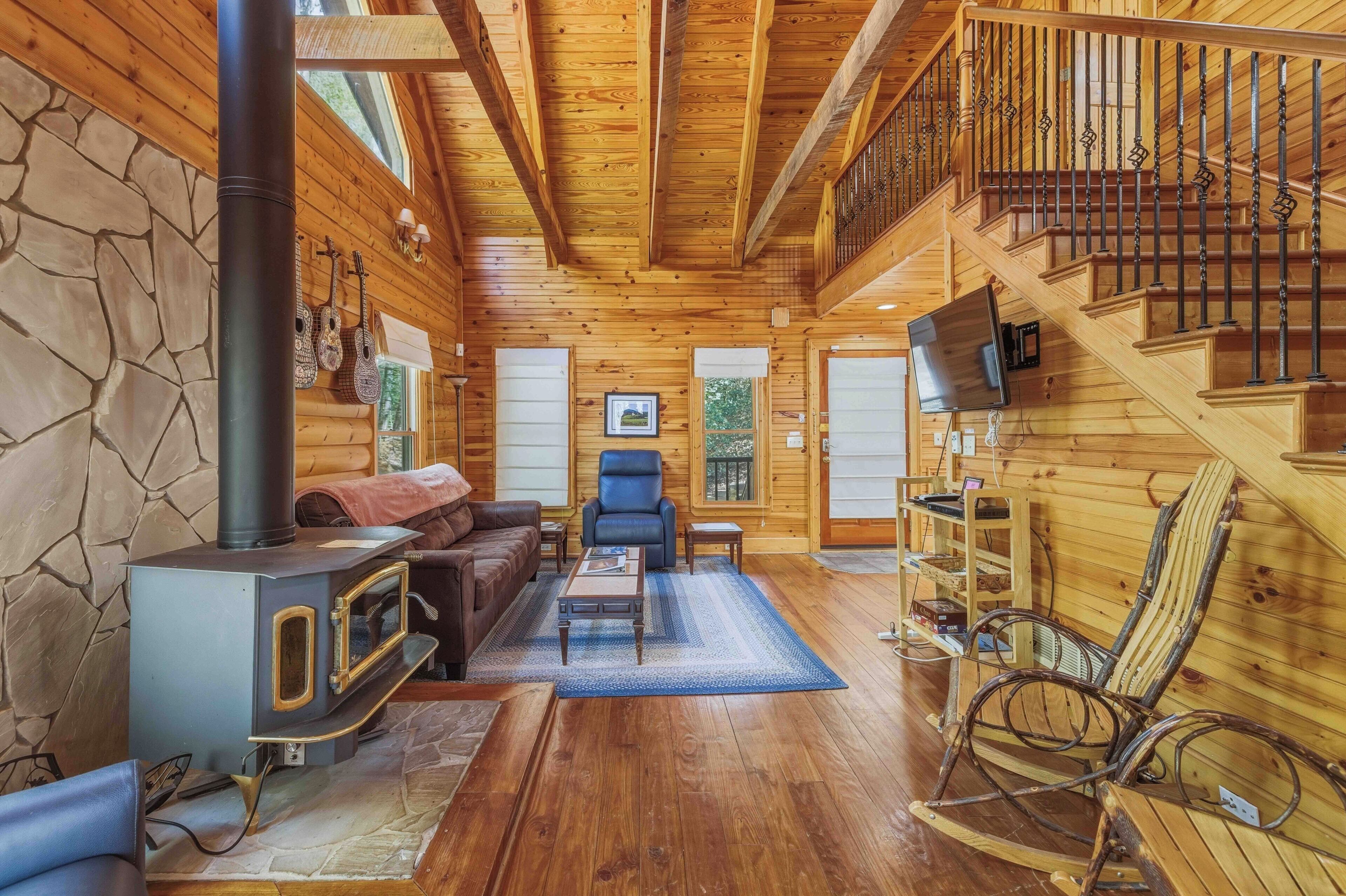 Een gezellig interieur van een chalet met een stenen muur, houten vloeren, een open haard, een bank, een fauteuil, een televisie en een trap.
