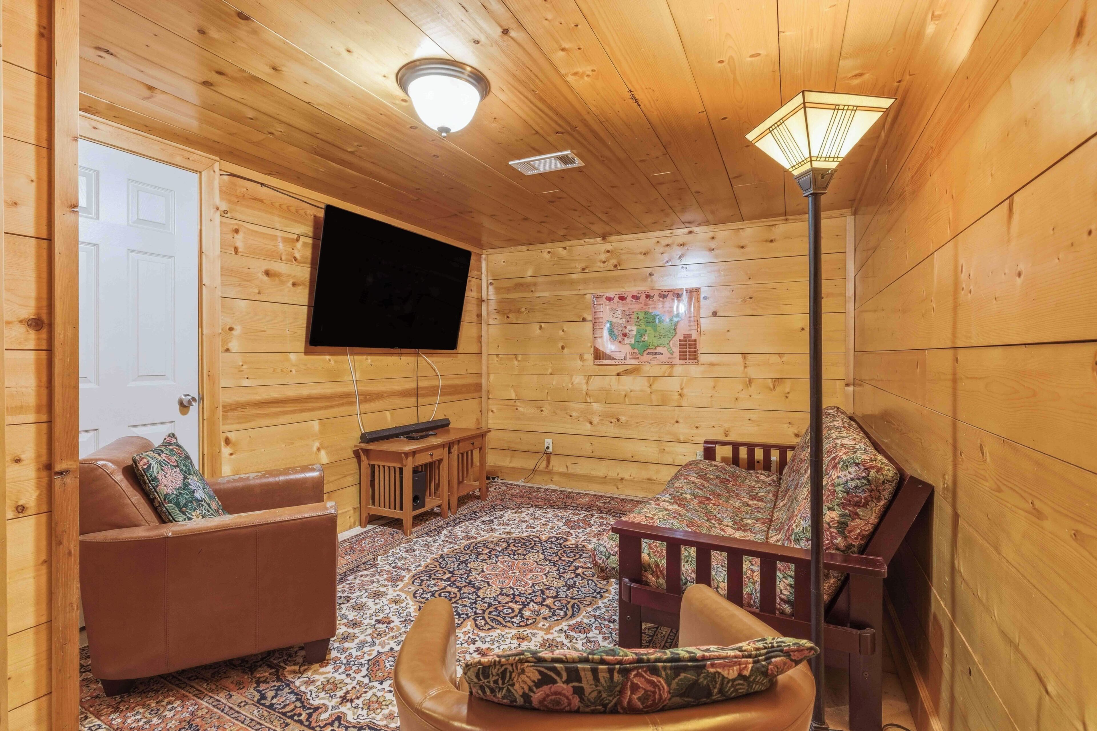 Un intérieur en bois avec un téléviseur à écran plat fixé au mur, un canapé, un tapis à motifs et un lampadaire en bois.