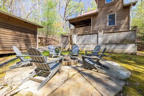 A wooden cabin with a fire pit and Adirondack chairs in the backyard.