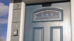 A blue door with a decorative glass panel and a numerical address sign.