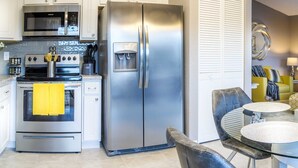 A modern kitchen with stainless steel appliances, a dining area with a glass table and chairs, and a living room with a sofa and decorative items.