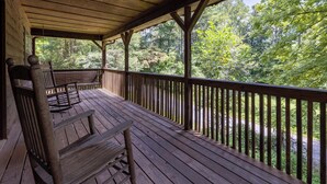 A wooden deck with a bench and railing, overlooking a forested area. - Country Charm A - Pet Friendly Group Cabin (Helen)