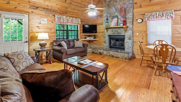 A cozy cabin interior with a stone fireplace, wooden walls, a leather sofa, and a television. - Country Charm A - Pet Friendly Group Cabin (Helen)