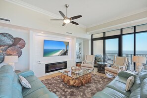 A spacious living room with a large TV, comfortable seating, and a view of the ocean.