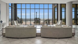 A spacious room with large windows offering a view of a beach and palm trees. There are two beige sofas and a small coffee table.