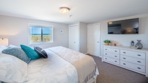 A bedroom with a bed, a dresser, a TV, and a window with a view.
