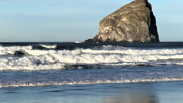 A beach with a large rock formation in the ocean.