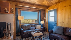A cozy cabin interior with a large window, leather sofas, a fireplace, and a blue door.
